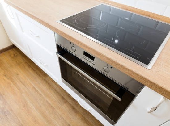 Modern cooking stove in white kitchen interior with tiled wall and wooden countertop, nobody