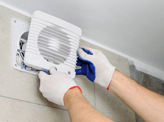 Installation of household appliances. Workman fixing the exhaust fan on the wall.